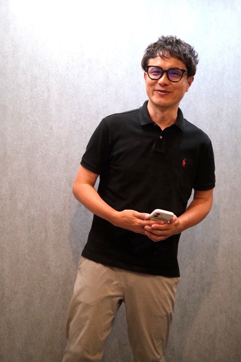 BB works代表 原口卓也 スマートフォンを手に笑顔で立っている写真